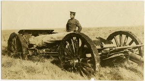 Horizontale sepiafoto van een man in uniform naast een artilleriekanon op wielen in een open veld